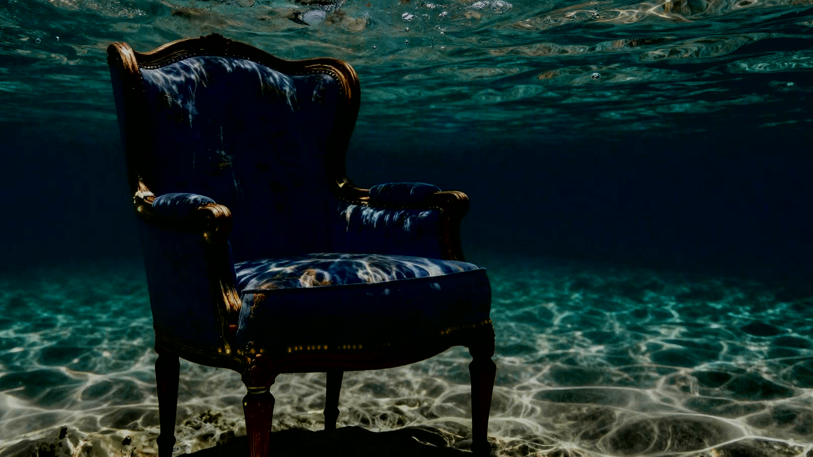 A dark blue wingback chair descending through deep ocean water